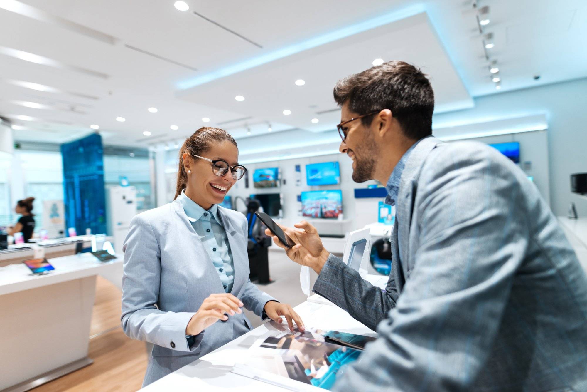Young multicultural couple looking for new smart phone to buy. Woman looking at catalog while man holding smart phone. Young multicultural couple looking for new smart phone to buy. Woman looking at catalog while man holding smart phone.