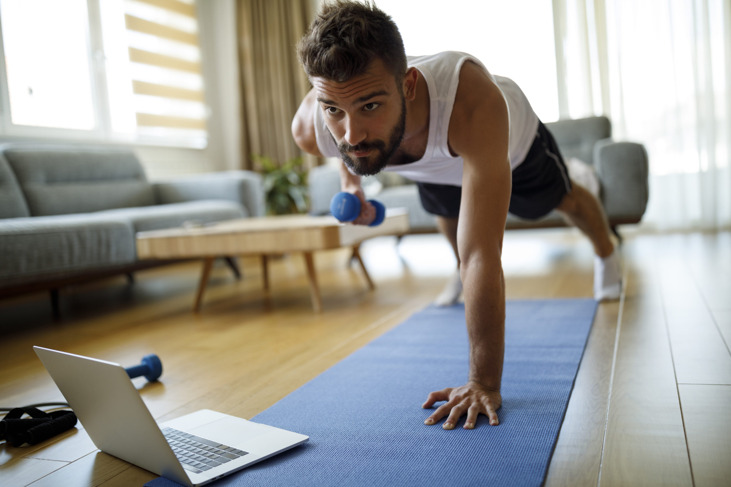 Young man using laptop and exercising at home